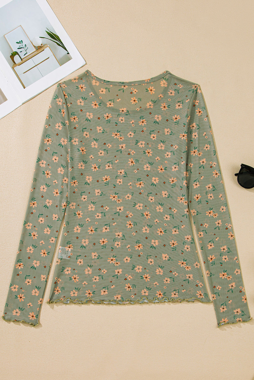 Green floral long-sleeve shirt on a beige surface with a magazine in the background