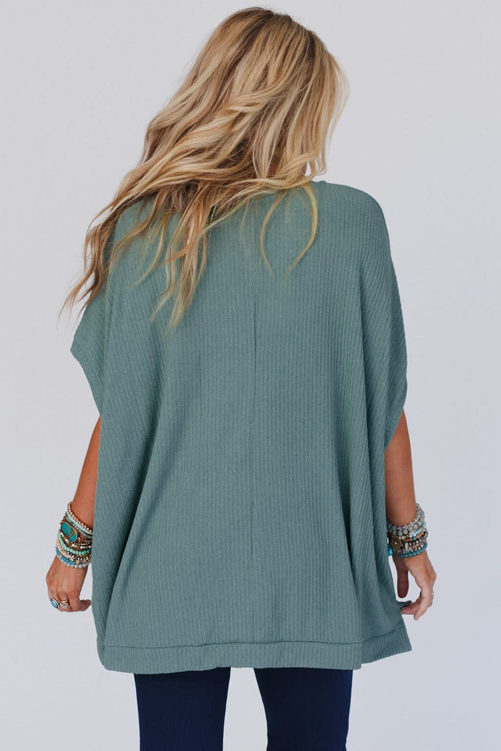Person wearing a teal poncho with long blonde hair and colorful bracelets on a white background