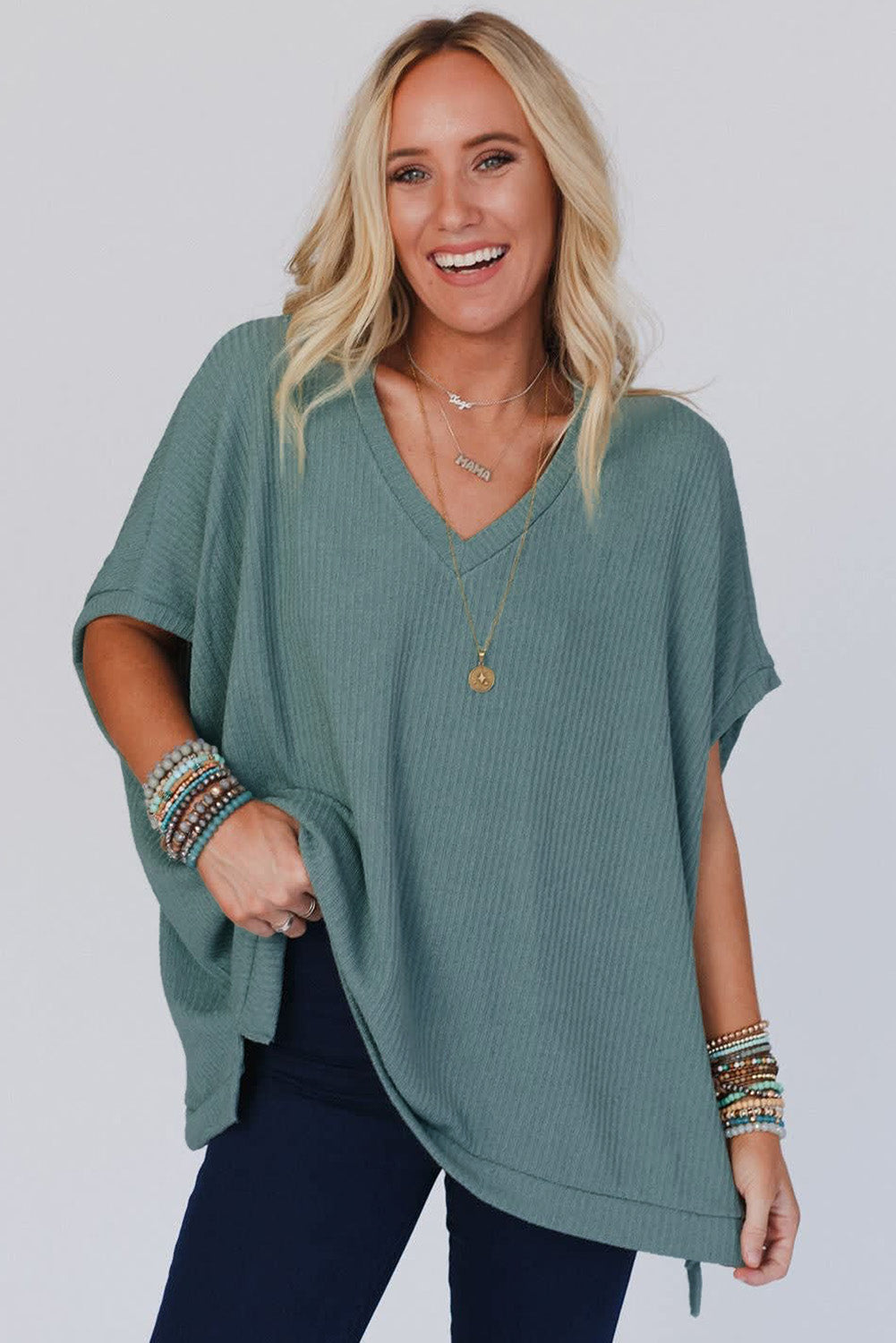 Woman wearing a teal oversized sweater with a plain background