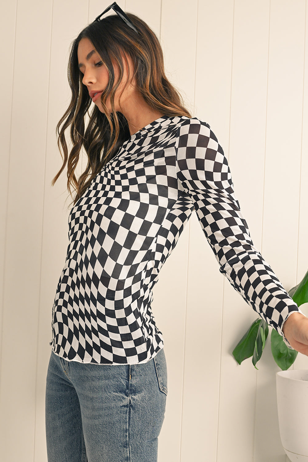 Woman wearing a black and white checkered long-sleeve top against a white wall.