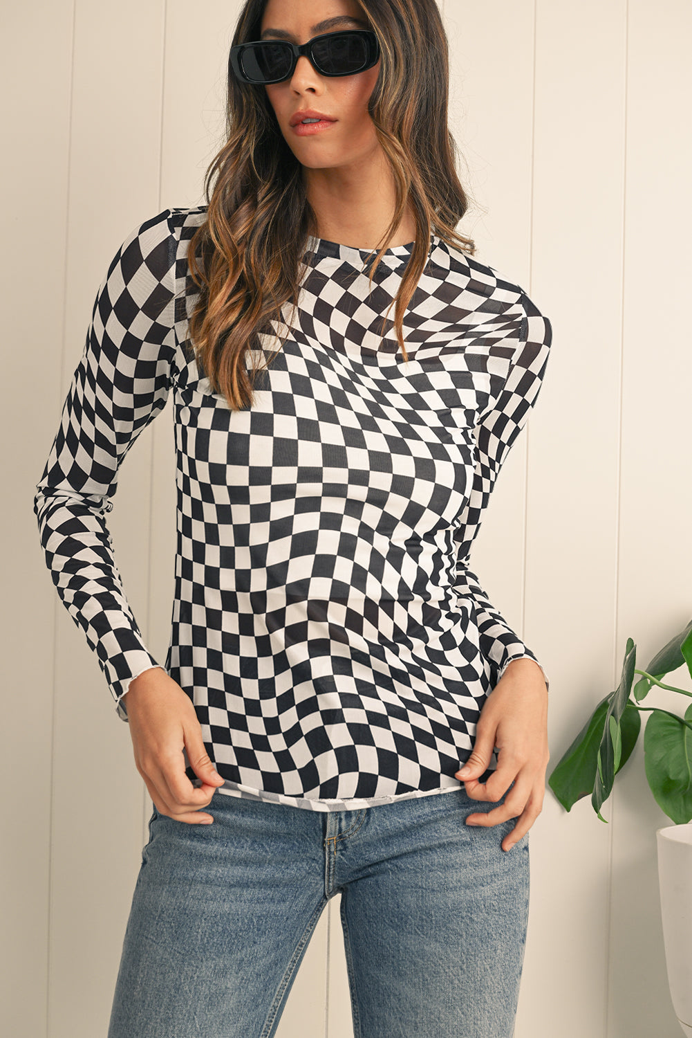 Woman wearing a black and white checkered long-sleeve top and blue jeans against a light background.