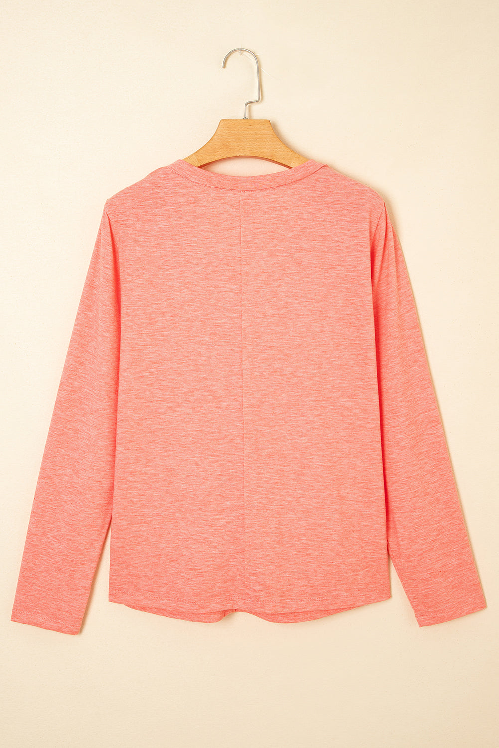 Pink long-sleeve shirt on a wooden hanger against a beige background