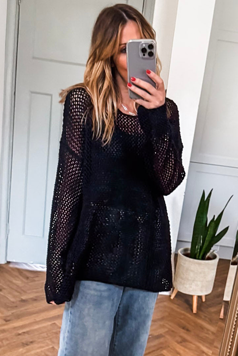 Woman taking a mirror selfie wearing a black knit sweater and light blue jeans.