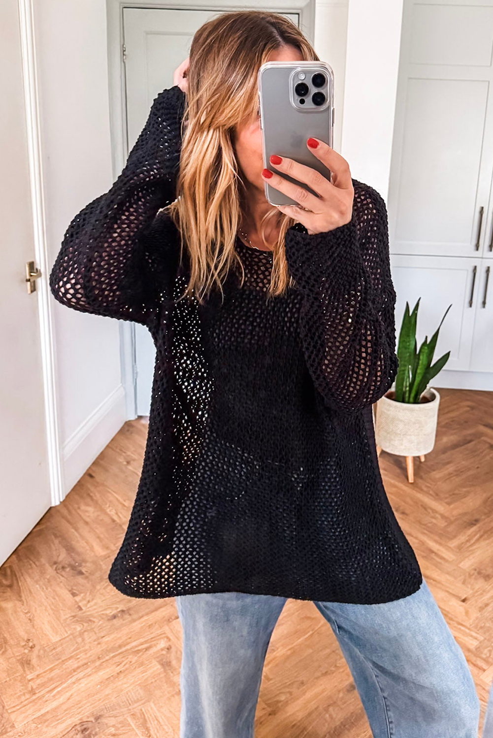 Person wearing a black knit sweater and light blue jeans, taking a mirror selfie.