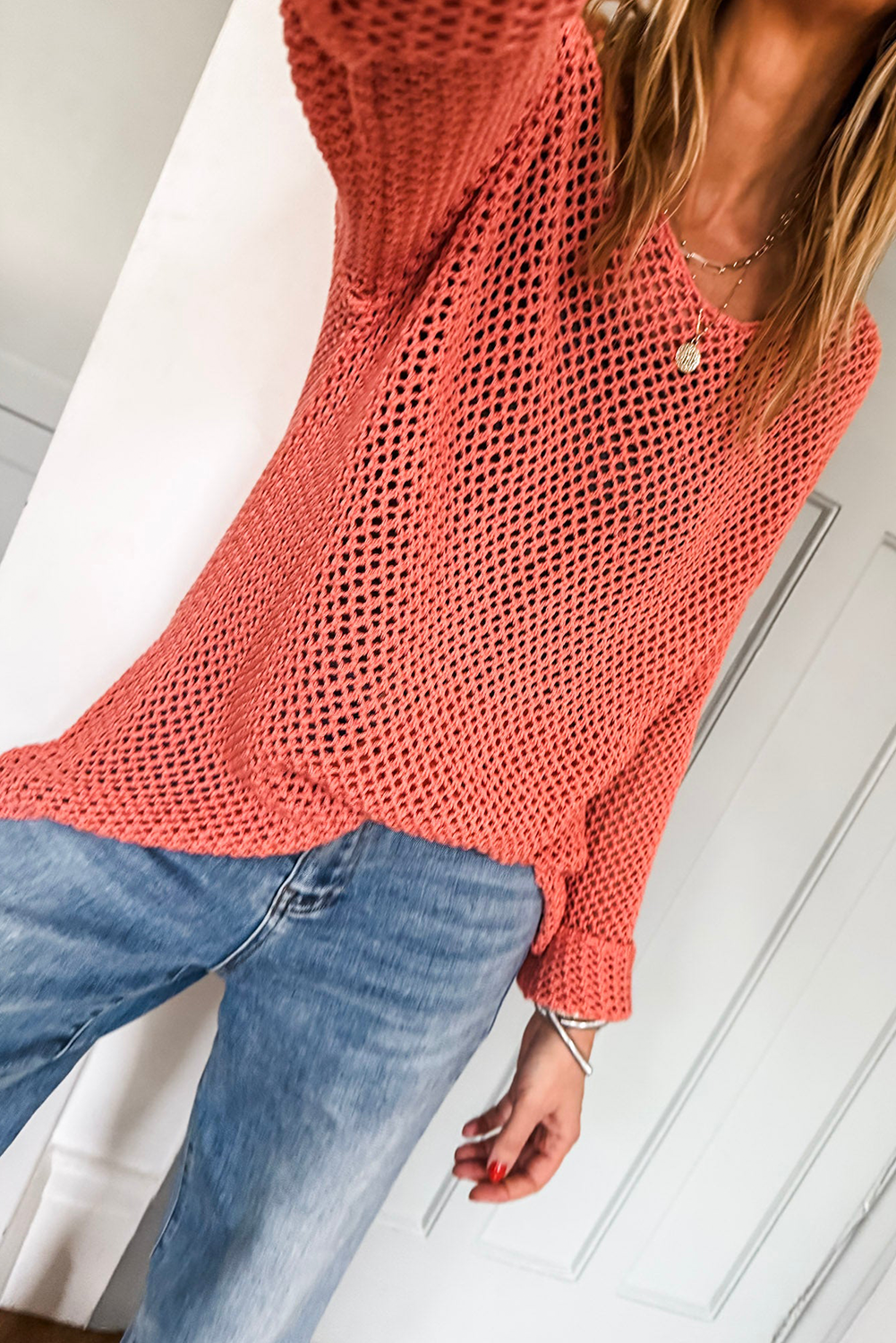 Person wearing a coral knit sweater and blue jeans indoors.