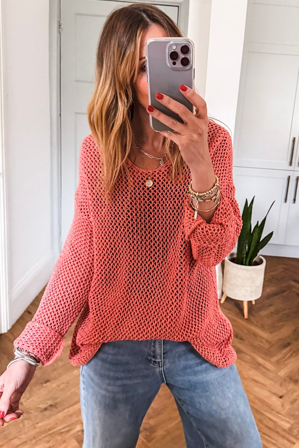 Woman wearing a pink knitted sweater and blue jeans, taking a mirror selfie.