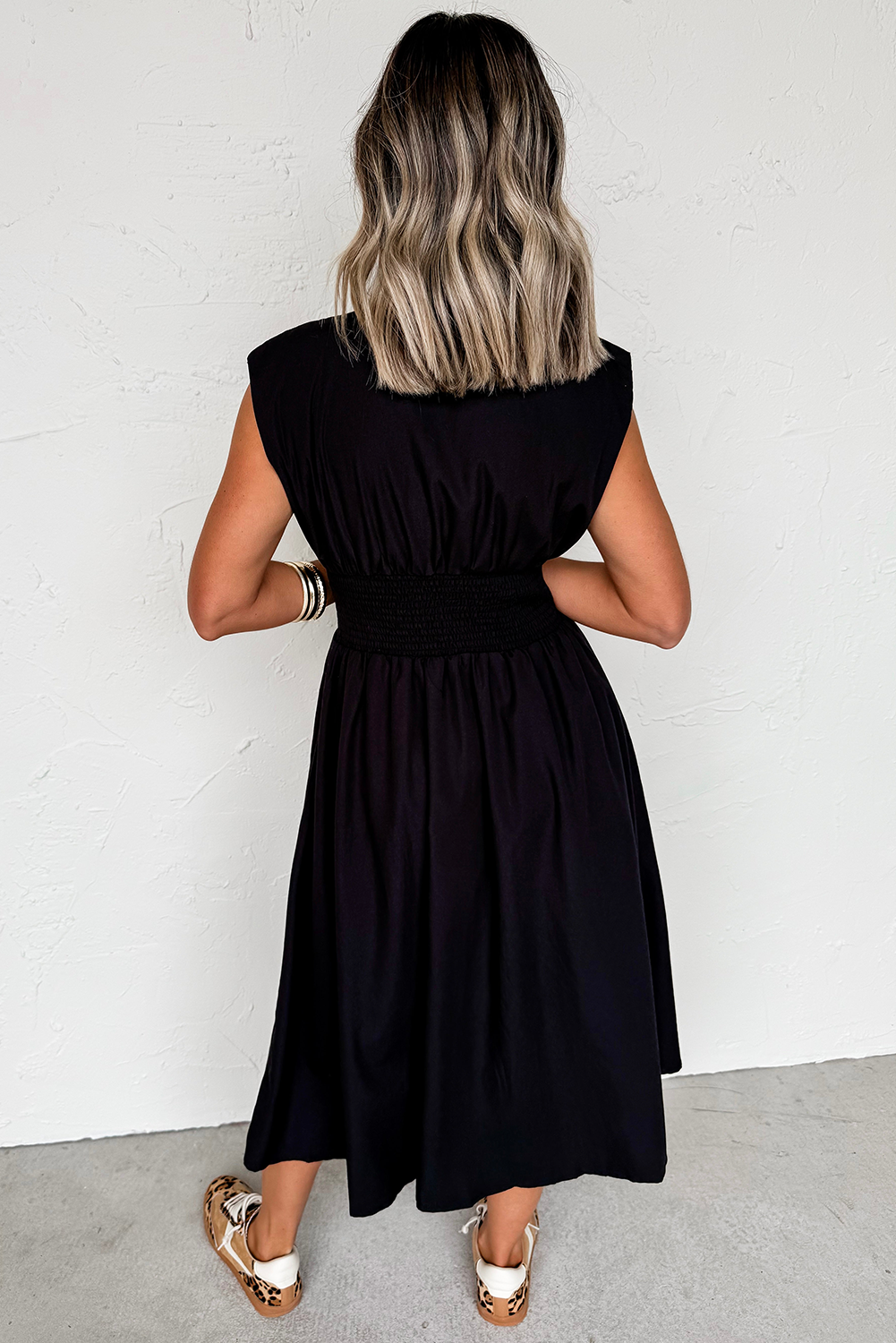 Person wearing a black sleeveless dress against a white wall