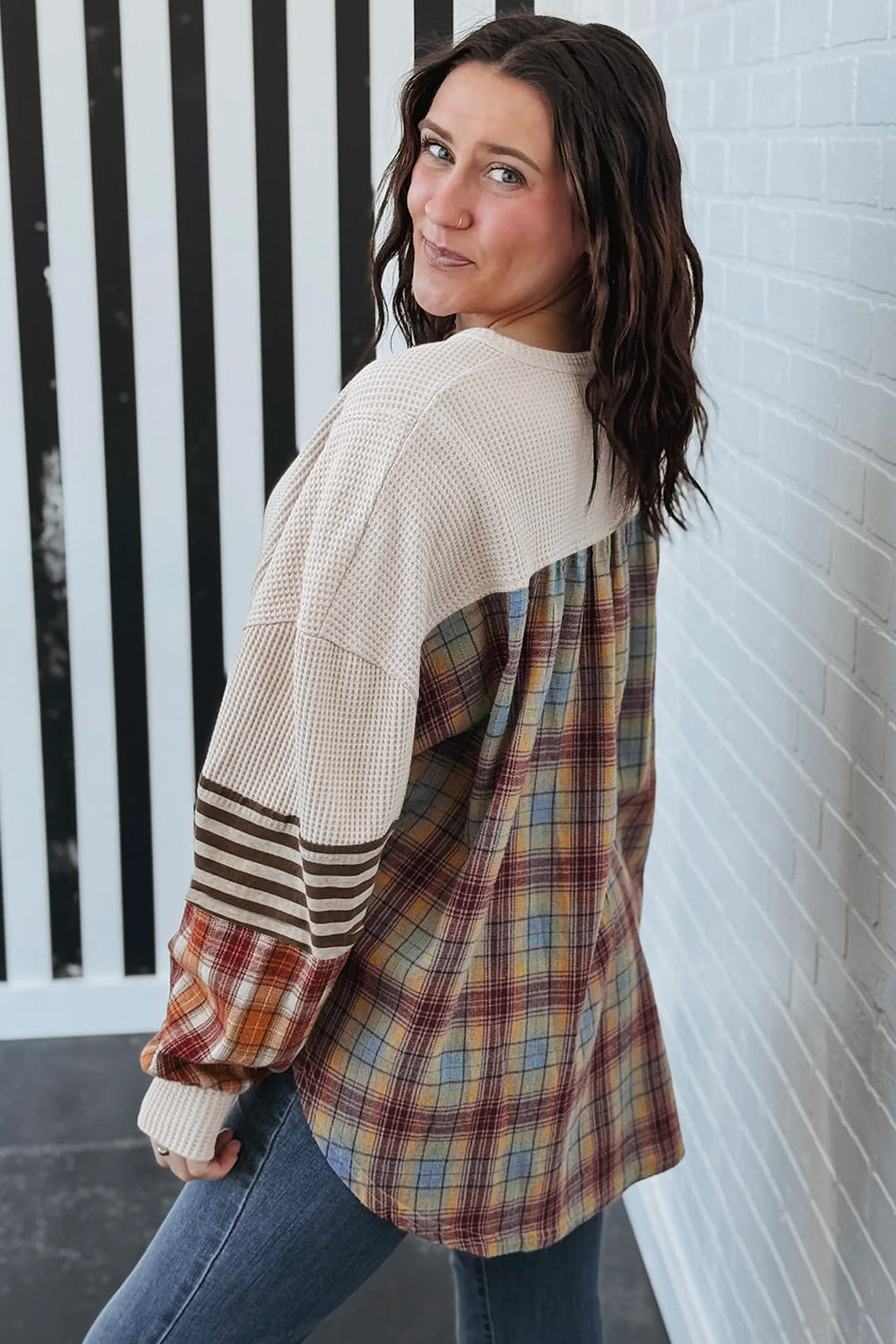 Woman wearing a plaid shirt over a beige sweater against a white wall.