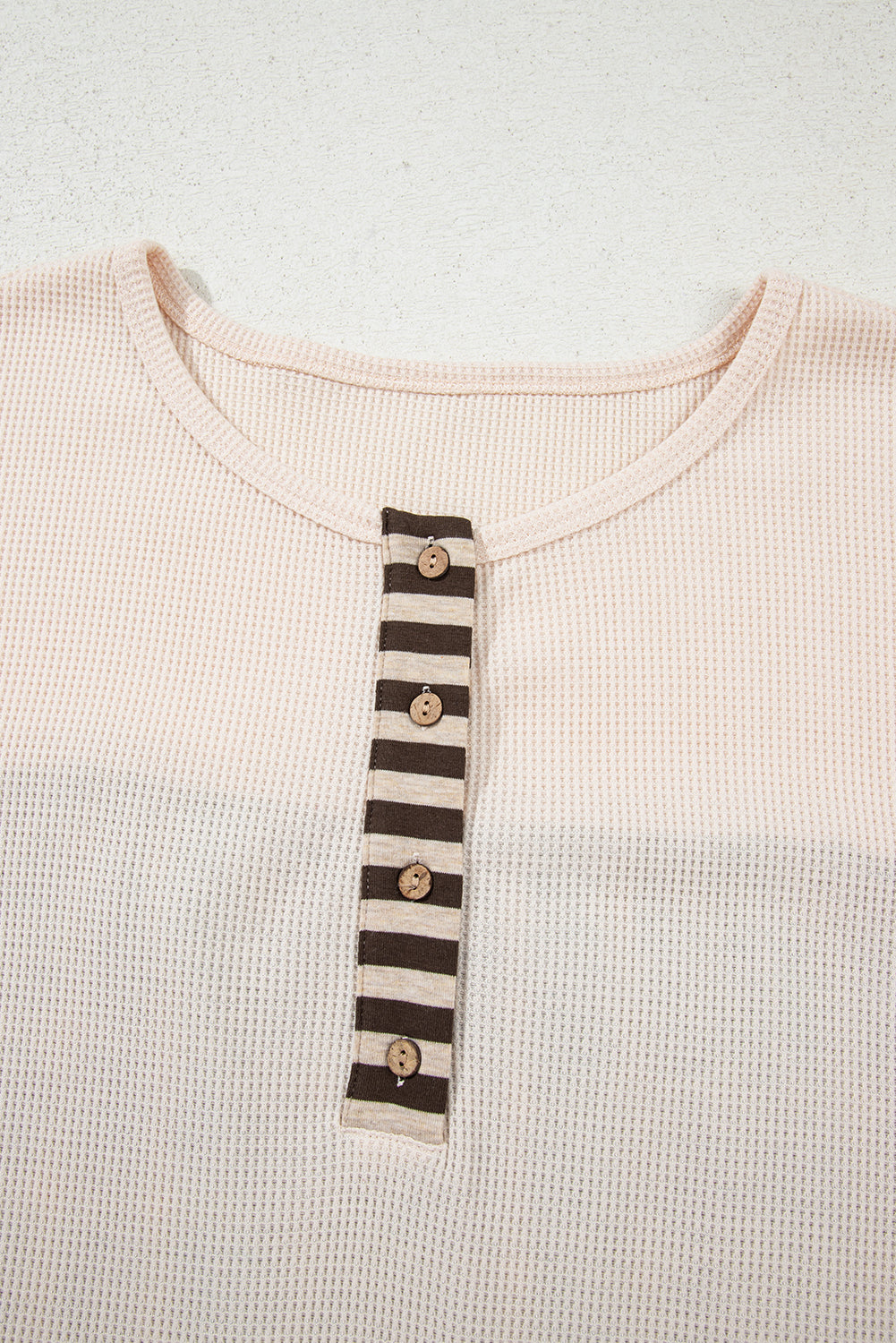 Close-up of a pink shirt with a striped collar and buttons on a light gray background