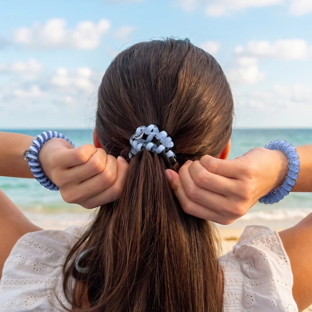 Doodlations Coffee Bar & Boutique blue spiral hair ties worn in a ponytail and as bracelets on a beach
