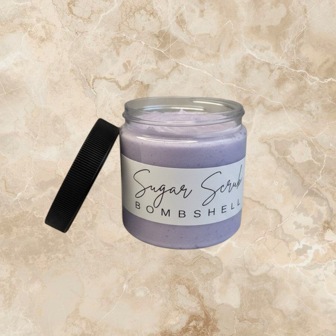 Doodlations Coffee Bar & Boutique Bombshell Sugar Scrub in a clear jar with a black lid. Lavender colored exfoliating scrub.