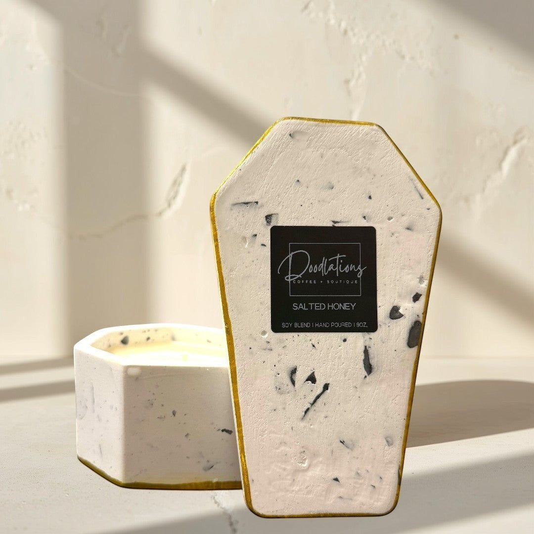 Doodlations Coffee Bar & Boutique casket-shaped concrete candle with dual wicks and a gold rim, filled with salted honey soy blend wax.