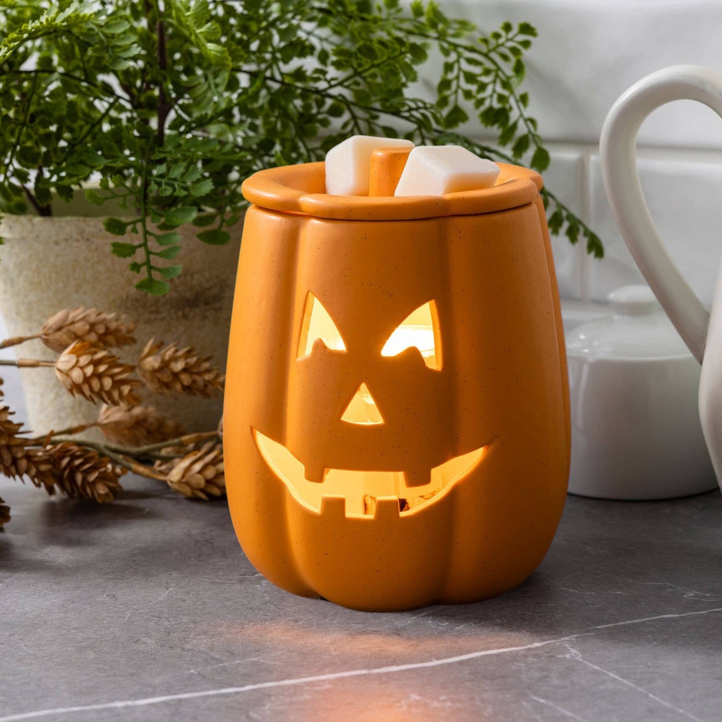 Doodlations Coffee Bar & Boutique orange ceramic jack-o'-lantern electric wax warmer with glowing face on a counter.