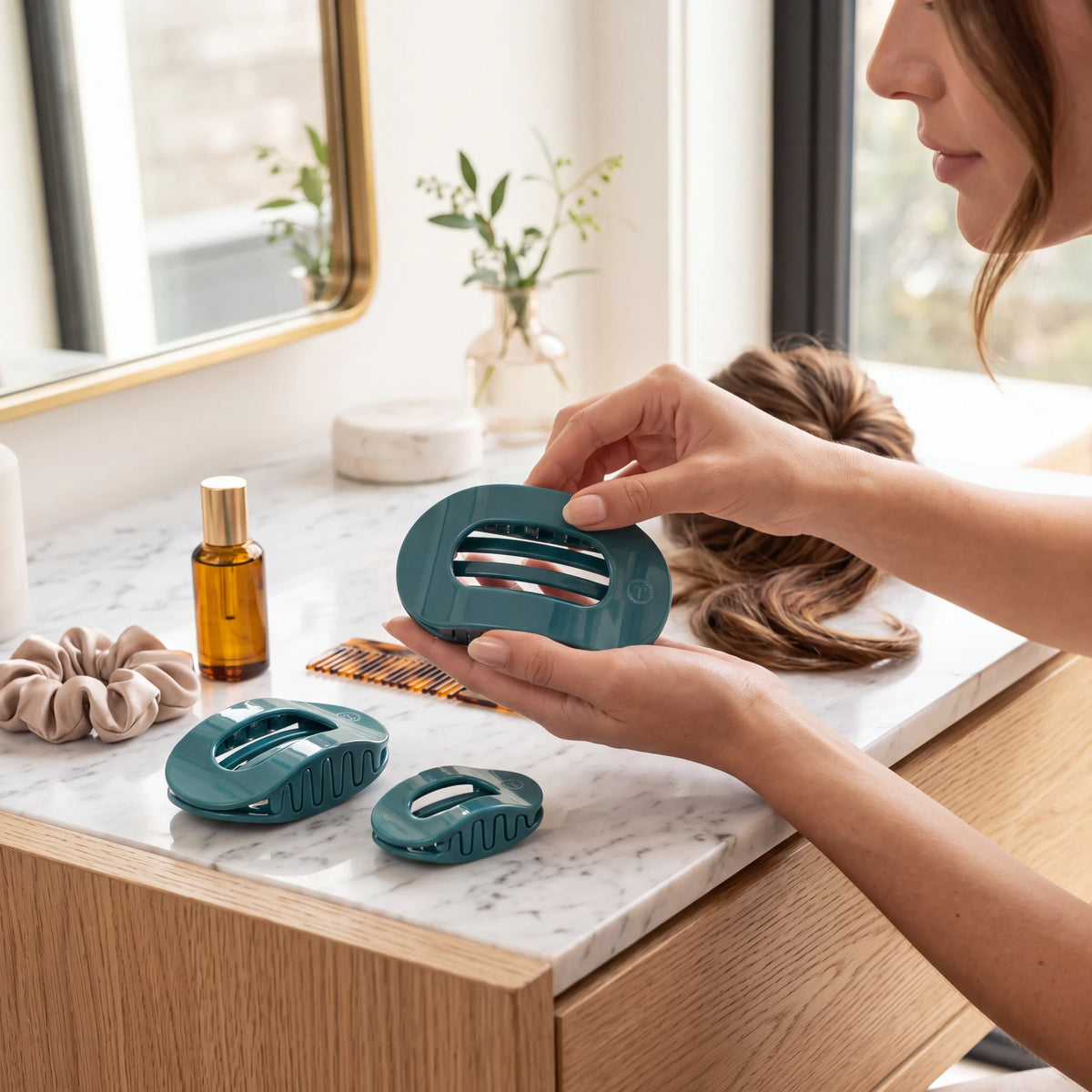 Doodlations Coffee Bar & Boutique teal flat round hair clip held by a woman on a marble vanity with accessories.