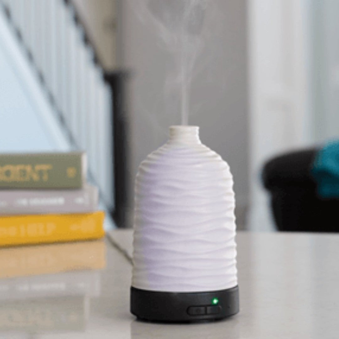 Doodlations Coffee Bar & Boutique white ceramic water droplet aroma diffuser with wavy texture emitting mist.