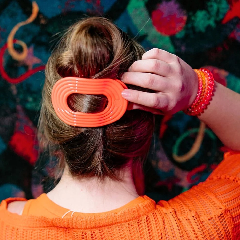 Doodlations Coffee Bar & Boutique orange ribbed flat oval hair clip securing a bun.