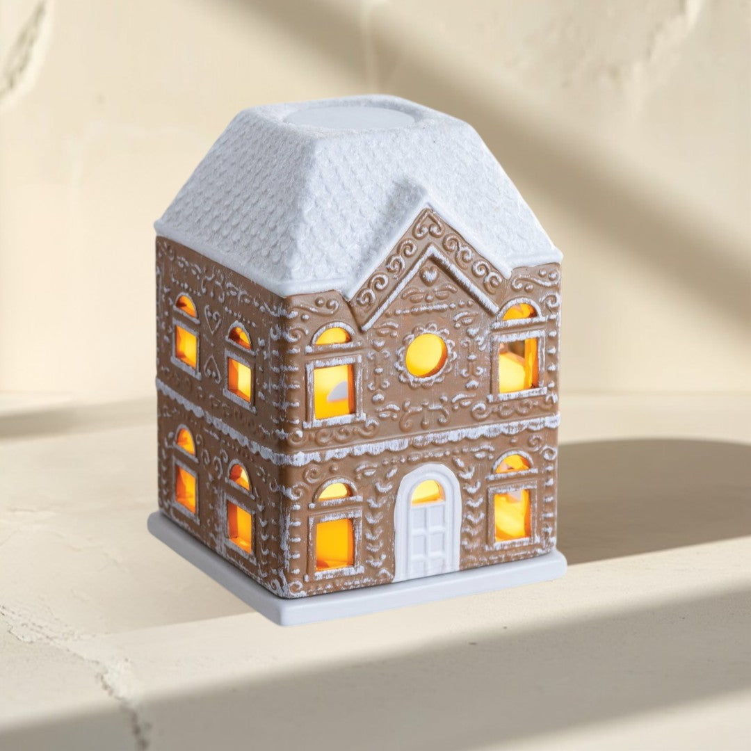 Gingerbread House Fragrance Warmer with white roof and illuminated windows.