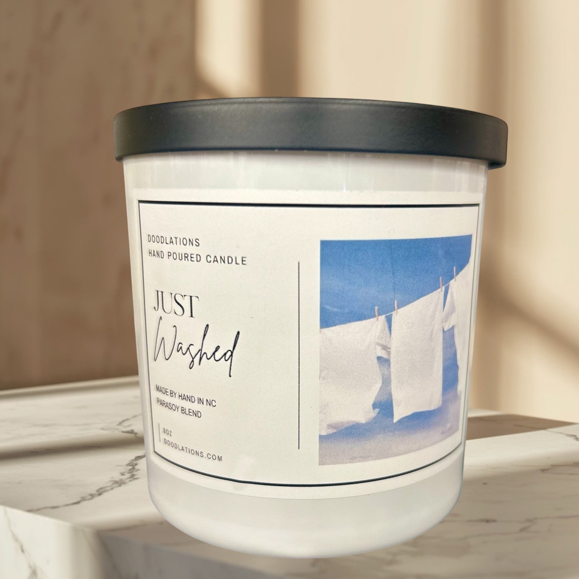 Just Washed candle with a clean laundry scent, featuring white sheets drying on a clothesline against a blue sky.