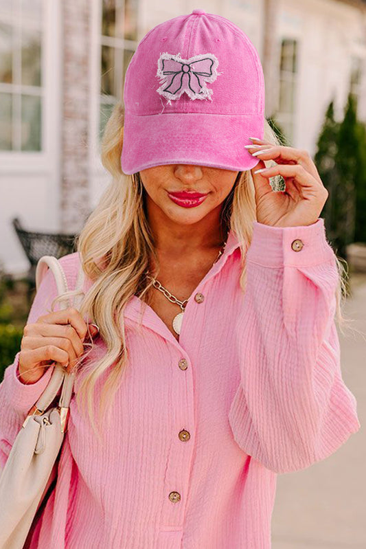 Woman wearing a pink cap with a bow design, pink shirt, and holding a beige handbag.