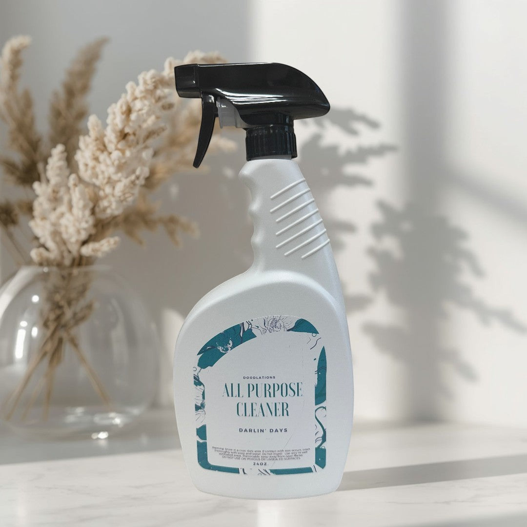 Darlin' Days All Purpose Cleaner spray bottle with a black trigger, on a marble surface with dried flowers in a vase.