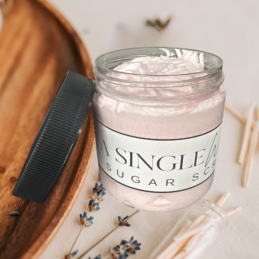 A Single Wish sugar scrub in a clear jar with a black lid. Pink scrub.