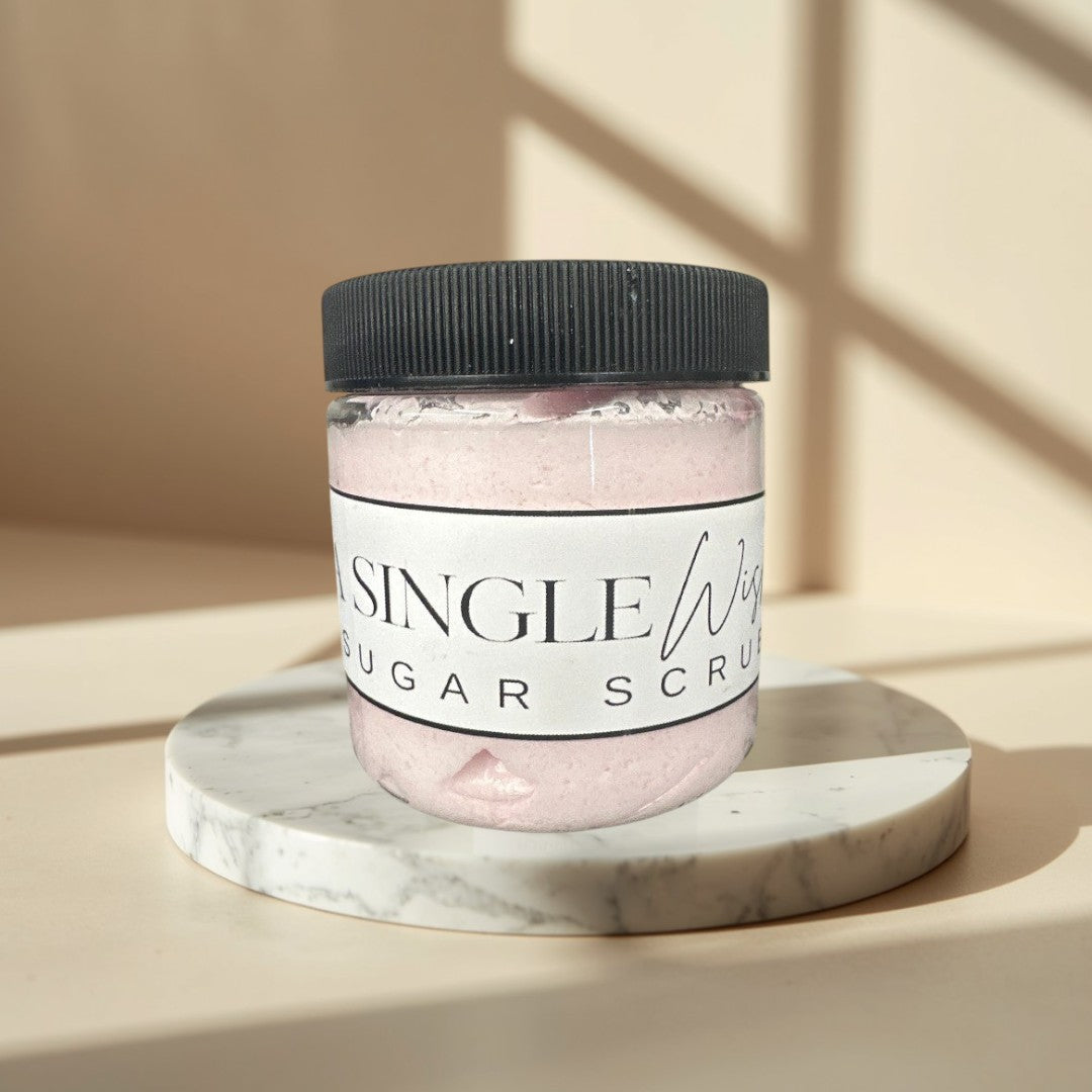 A Single Wish sugar scrub in a clear jar with a black lid. Pink scrub.