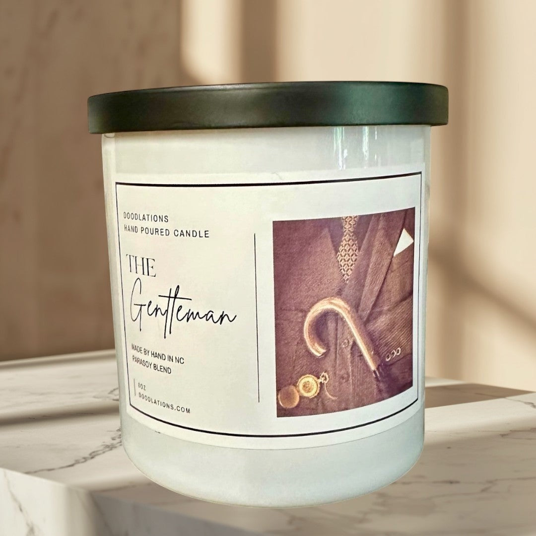 The Gentleman luxury soy blend candle with masculine cologne scent. Features a suit, tie, cane, and monocle.