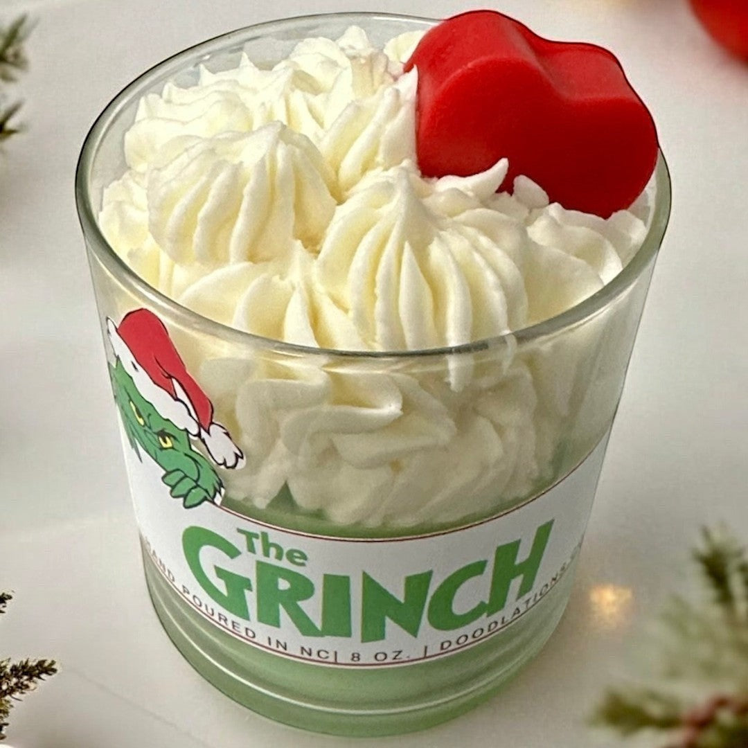 The Grinch candle with green wax and white whipped wax topping, decorated with a Grinch sticker and red heart.