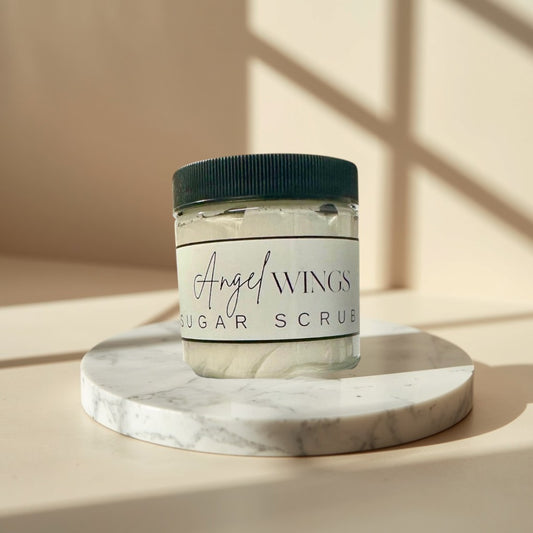 Angel Wings sugar scrub in clear jars with black lids. White scrub with visible sugar crystals.