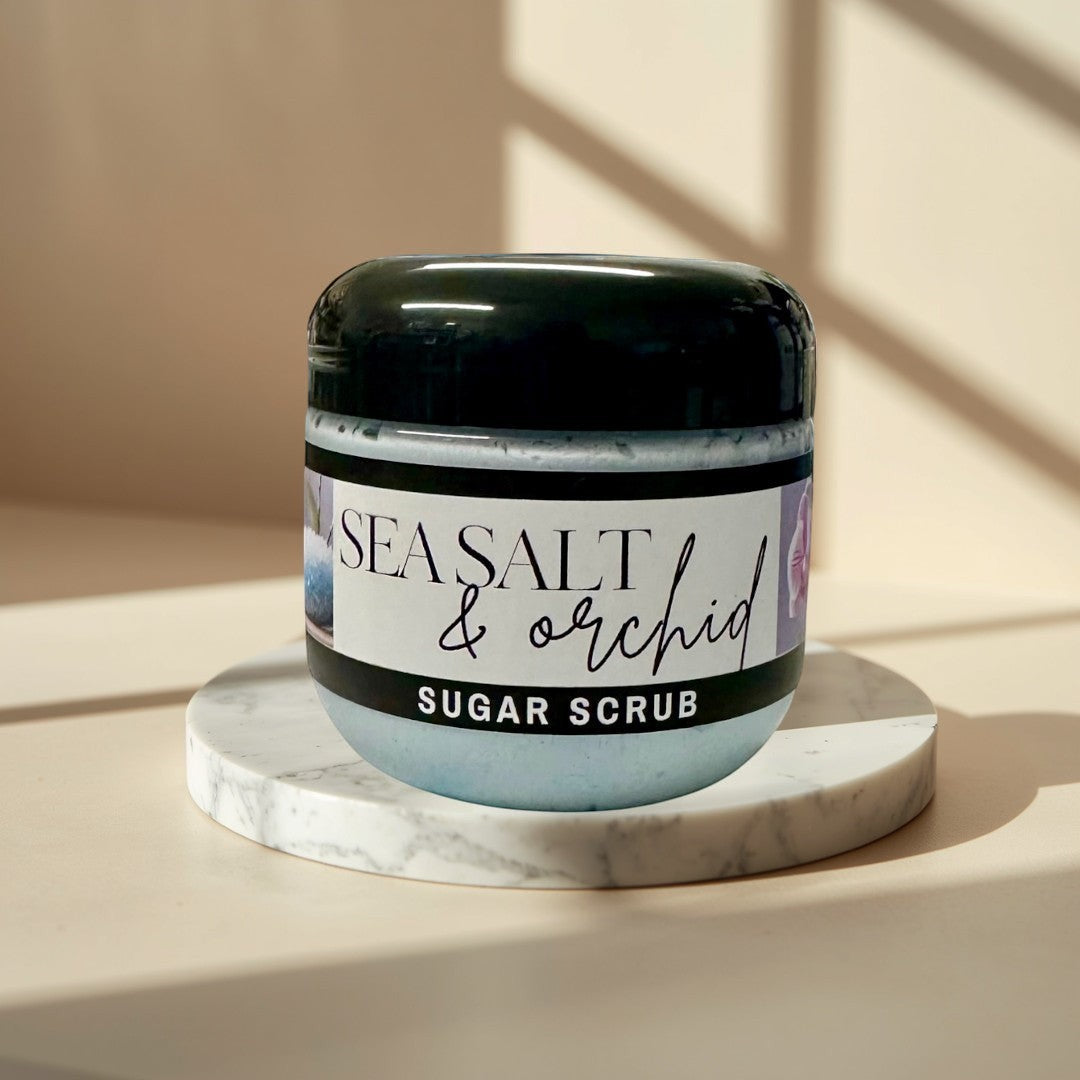 Sea Salt & Orchid Sugar Scrub in a clear jar with a black lid, light blue scrub inside.