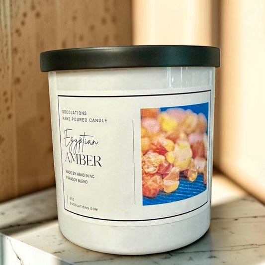 Doodlations Egyptian Amber hand-poured soy blend candle in a white jar with a black lid.
