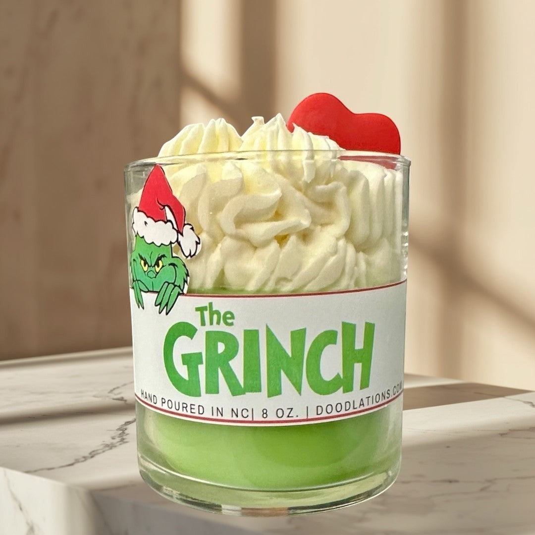 The Grinch candle with green wax and white whipped wax topping, decorated with a Grinch sticker and red heart.
