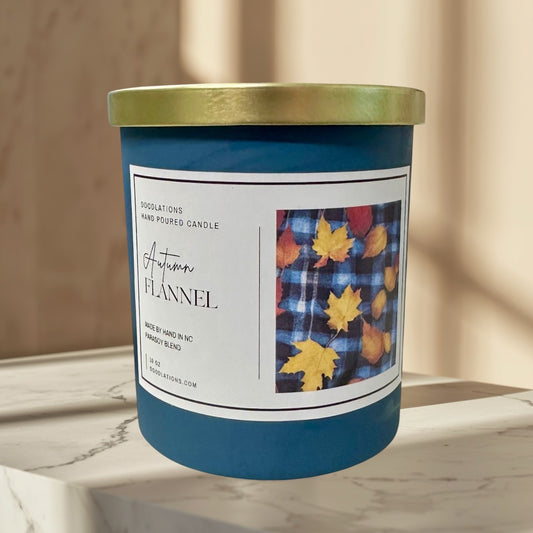 Doodlations Autumn Flannel hand-poured soy blend candle in a teal jar with a gold lid. Features a label with plaid and fall leaves.