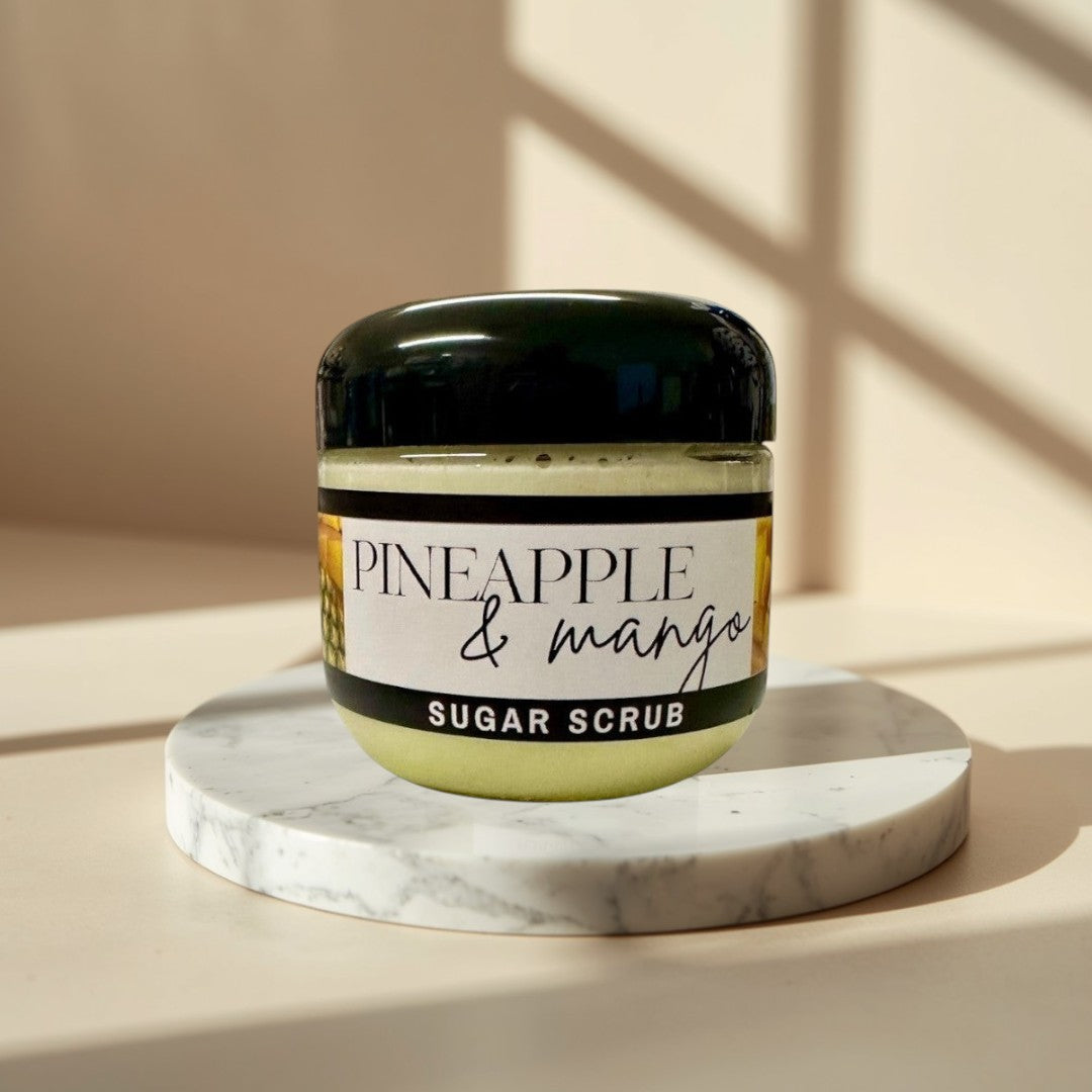 Pineapple Mango Sugar Scrub, a pale yellow exfoliating scrub in a clear jar with a black lid.