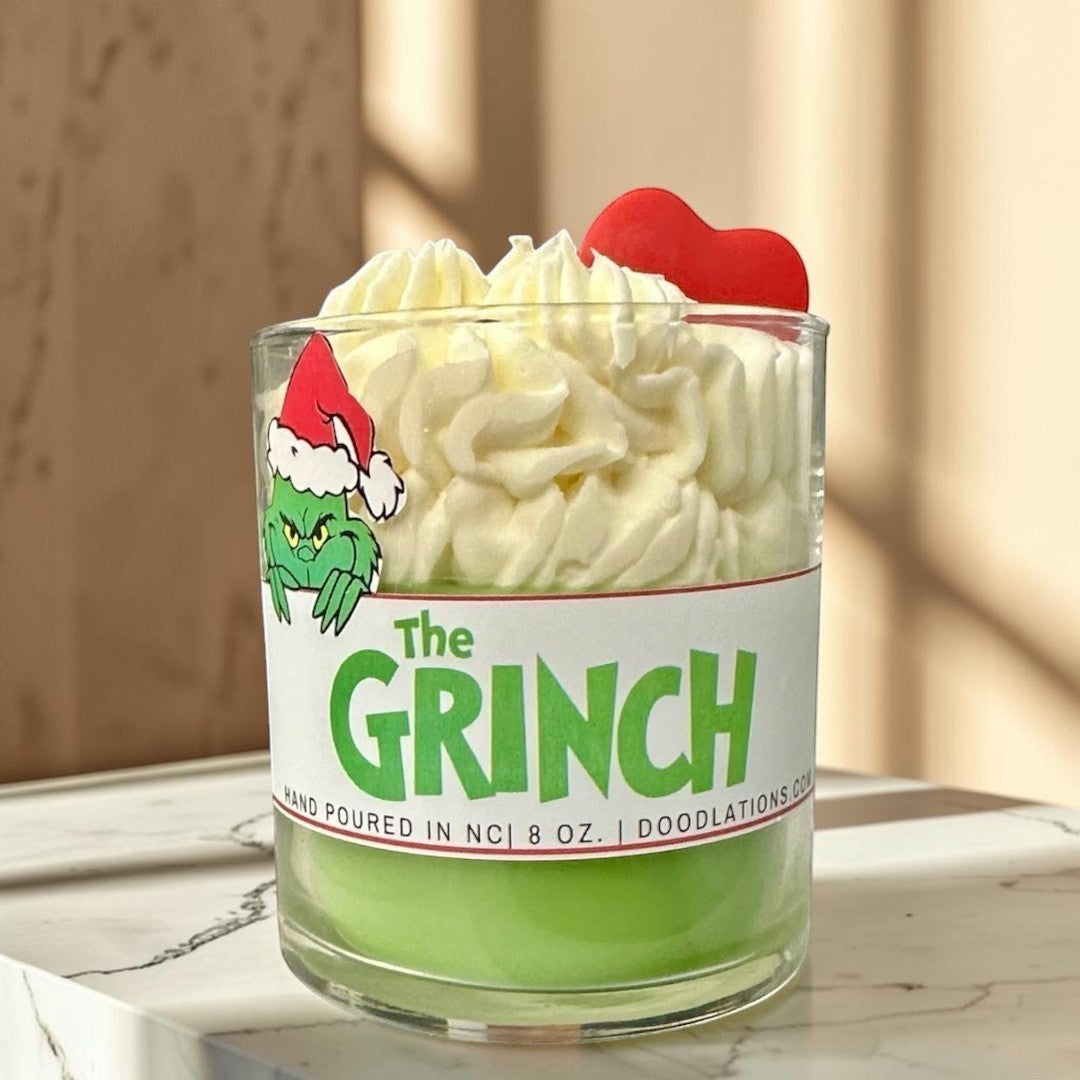 The Grinch candle with green wax and white whipped wax topping, decorated with a Grinch sticker and red heart.