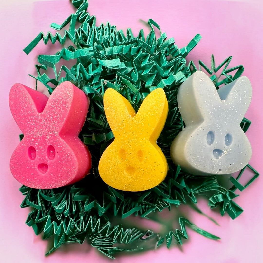 Peeps wax melts in pink, yellow, and blue bunny shapes with glitter, nestled in green crinkle paper.