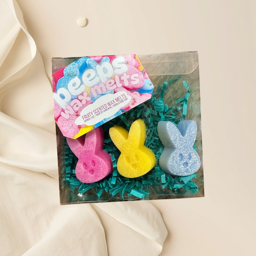 Peeps wax melts in pink, yellow, and blue bunny shapes with glitter, nestled in green crinkle paper.