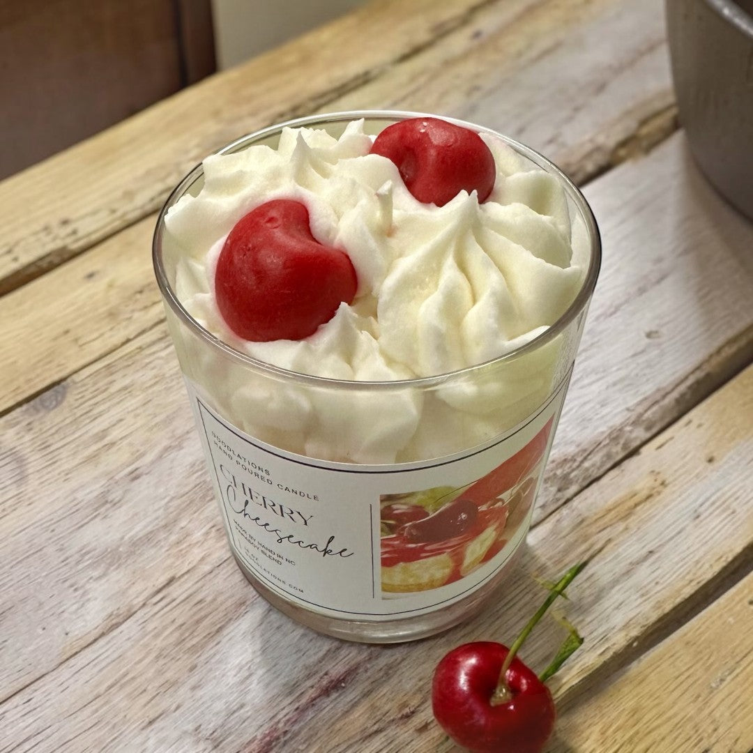 Cherry Cheesecake candle in a glass jar, resembling dessert with white cream and red drizzle.