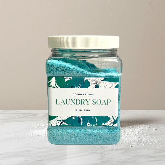 Doodlations Luxury Laundry Soap Bum Bum, a blue granular detergent in a clear plastic jar with a white lid.