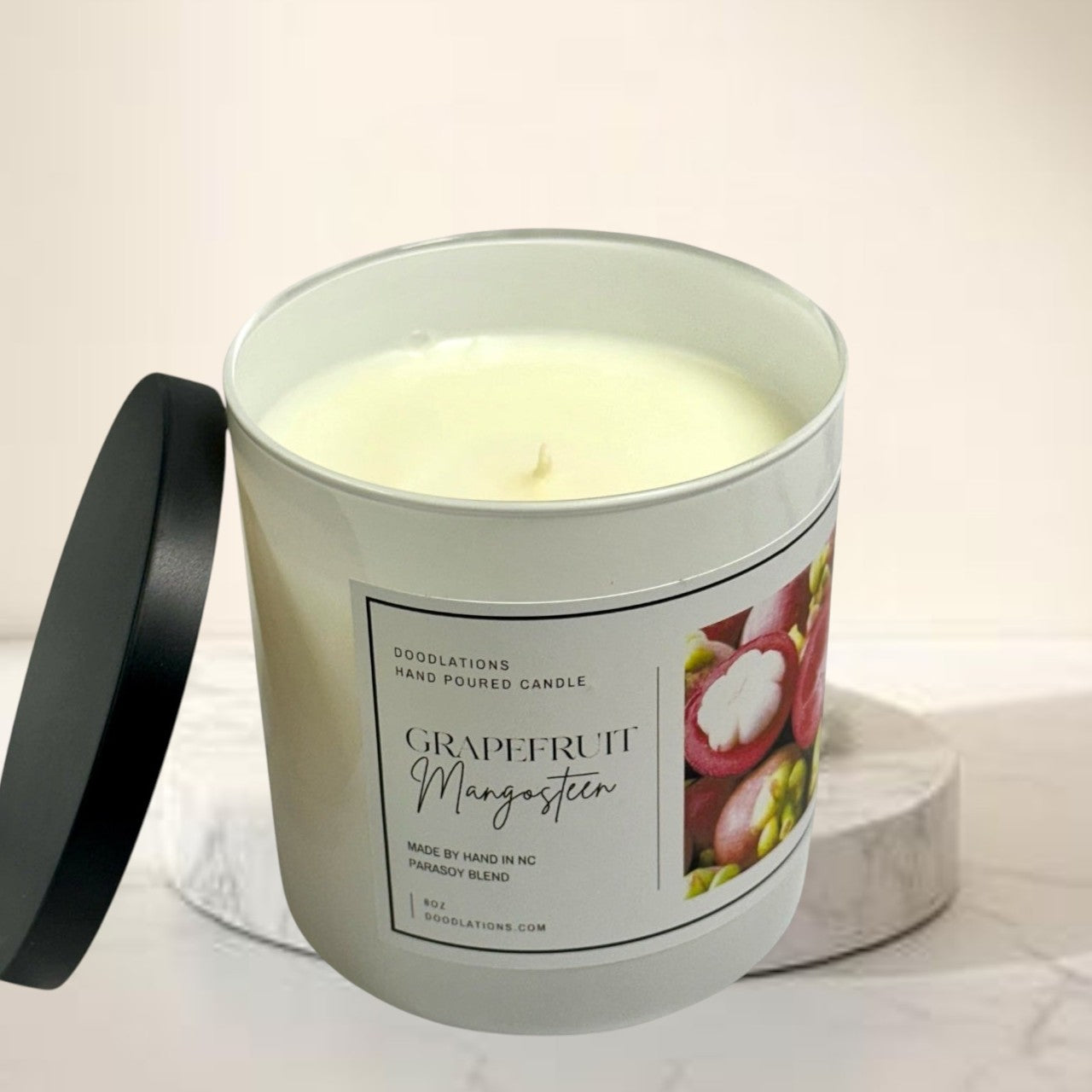 Grapefruit & Mangosteen hand-poured candle in a white jar with a black lid. Features a label with fruit imagery.