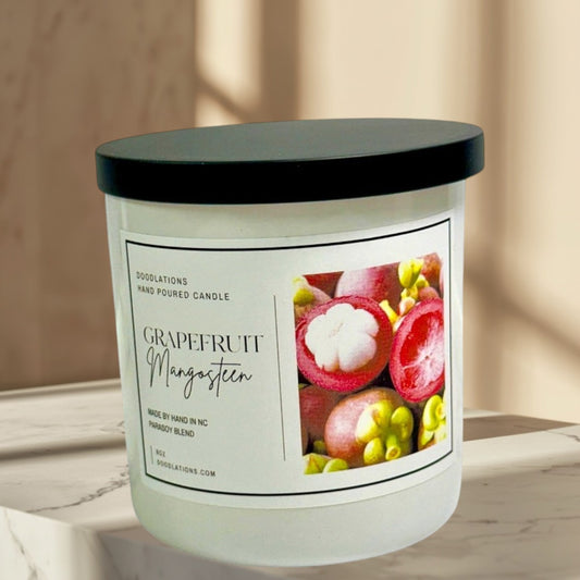 Grapefruit & Mangosteen hand-poured candle in a white jar with a black lid. Features a label with fruit imagery.