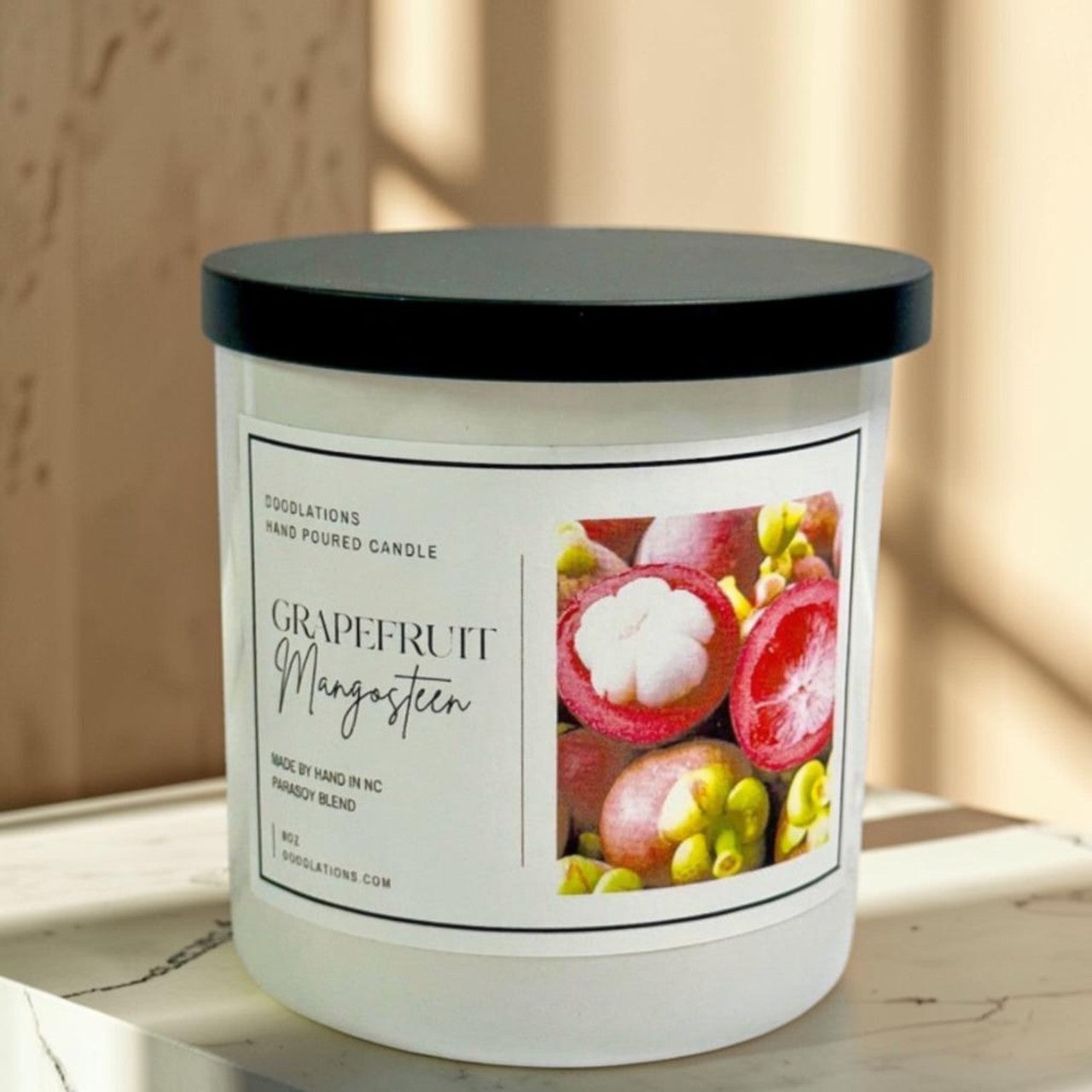 Grapefruit & Mangosteen hand-poured candle in a white jar with a black lid. Features a label with fruit imagery.