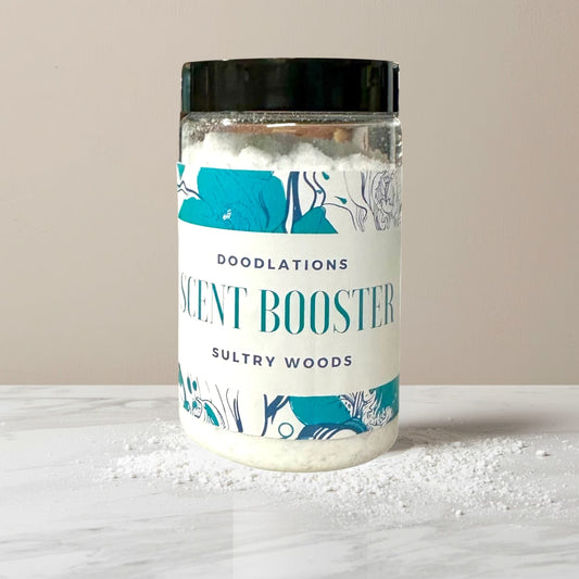 Doodlations Coffee Bar & Boutique Sultry Woods laundry scent booster in a clear plastic jar with a black lid. White granules fill the jar.