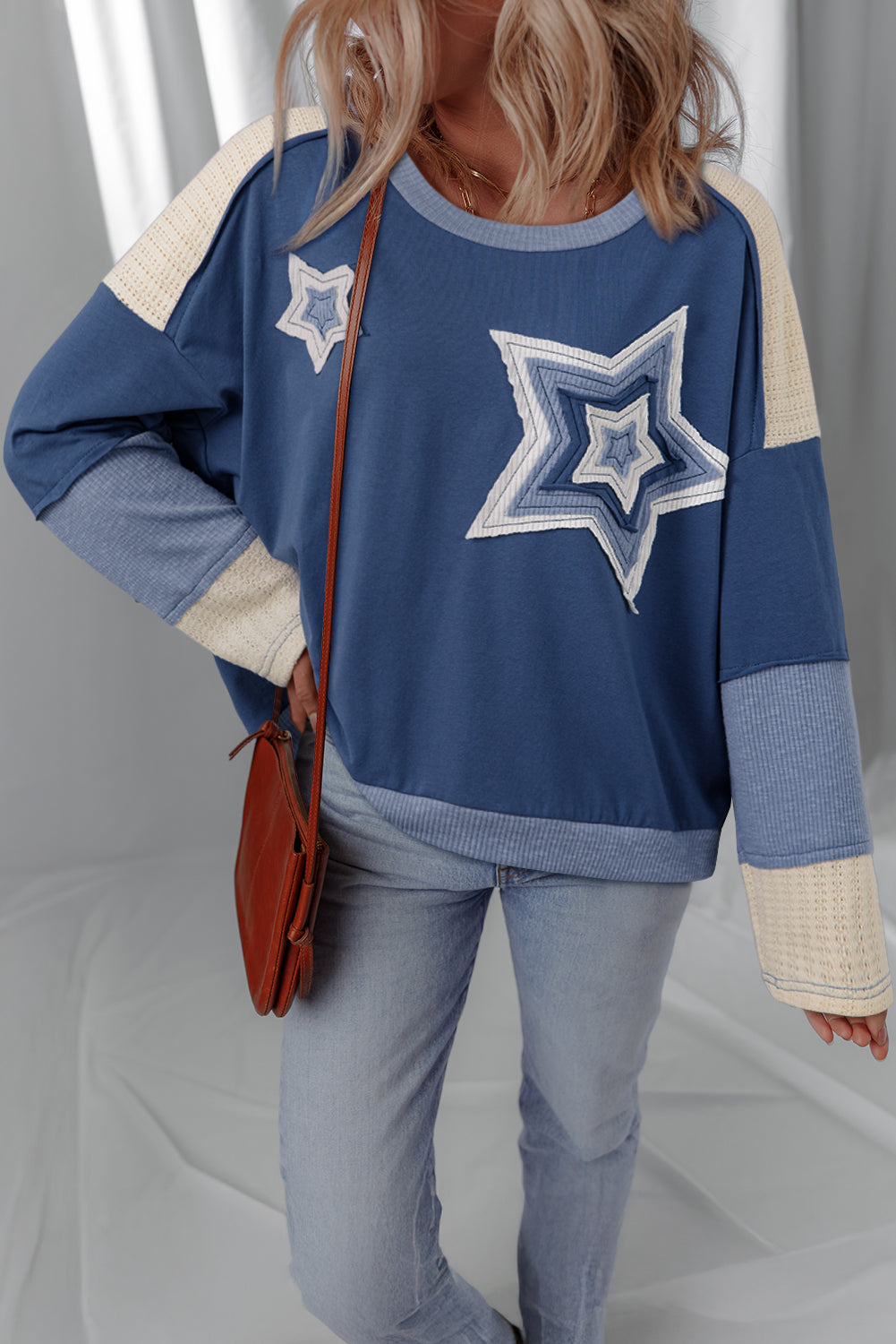 Person wearing a blue sweater with star designs and holding a brown bag.