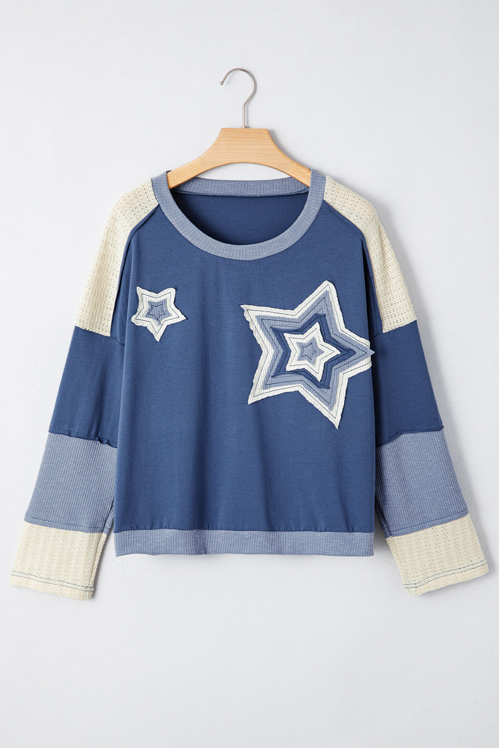 Blue sweater with star designs on a hanger against a white background