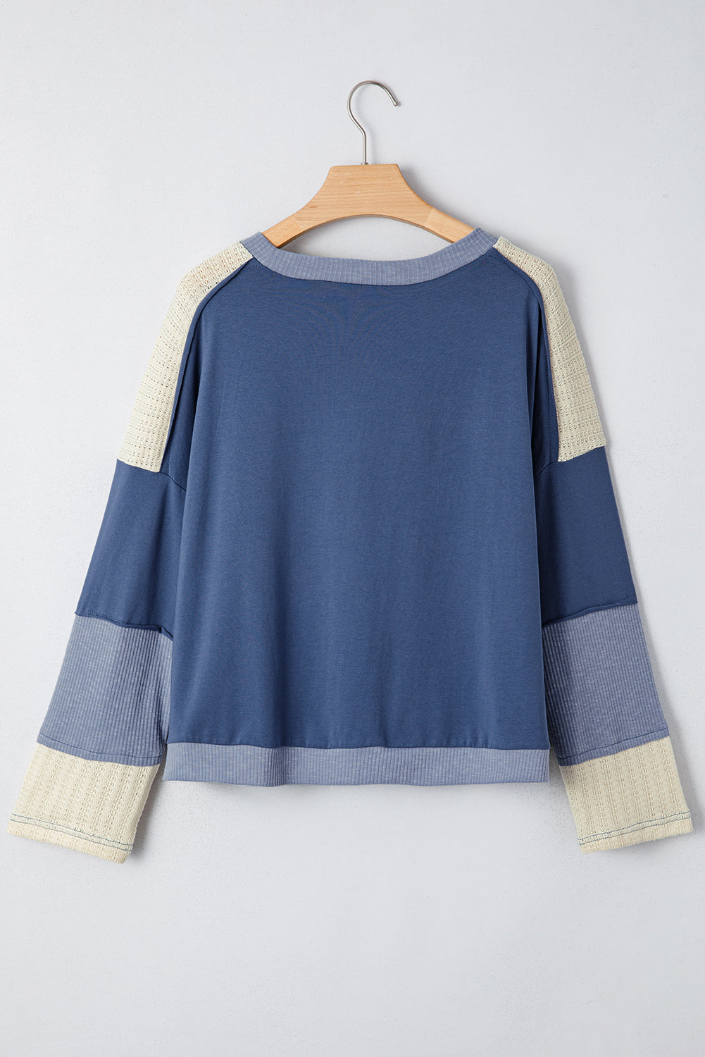 Blue sweater with beige cuffs and hem on a hanger against a white background