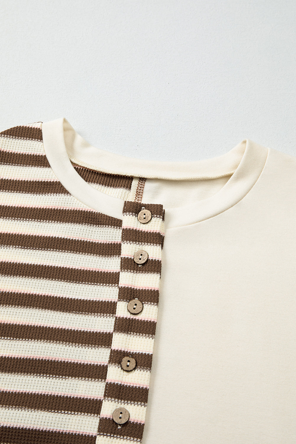 Close-up of a baby outfit with brown and white striped pattern and buttons on a light gray background