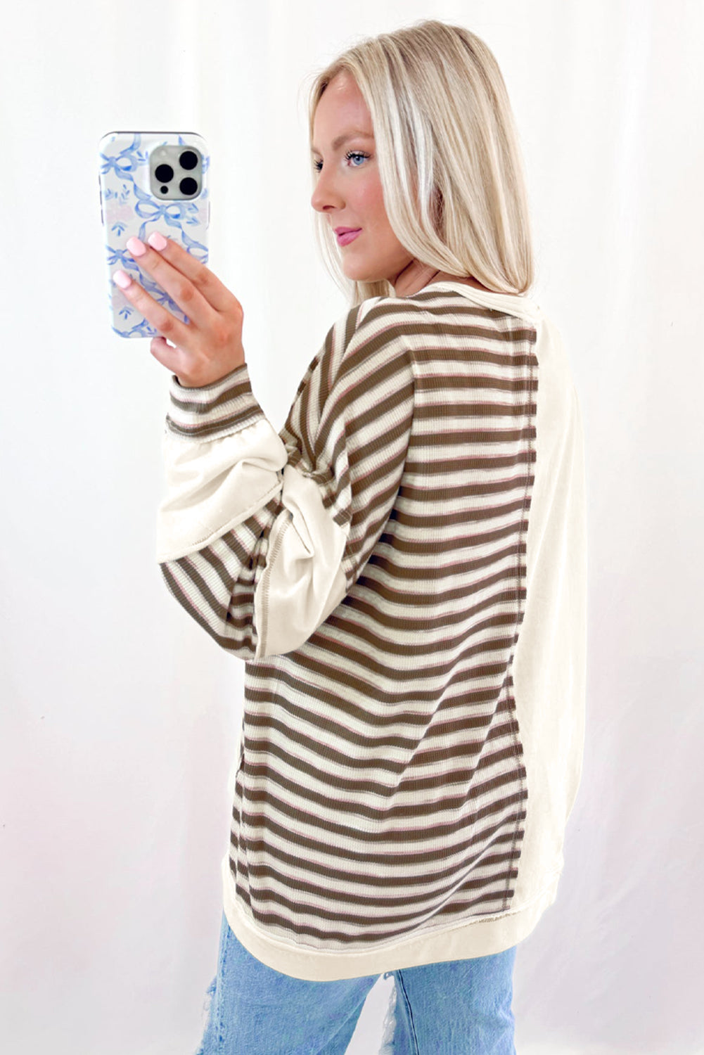 Woman wearing a brown and beige striped sweater holding a phone with a white background