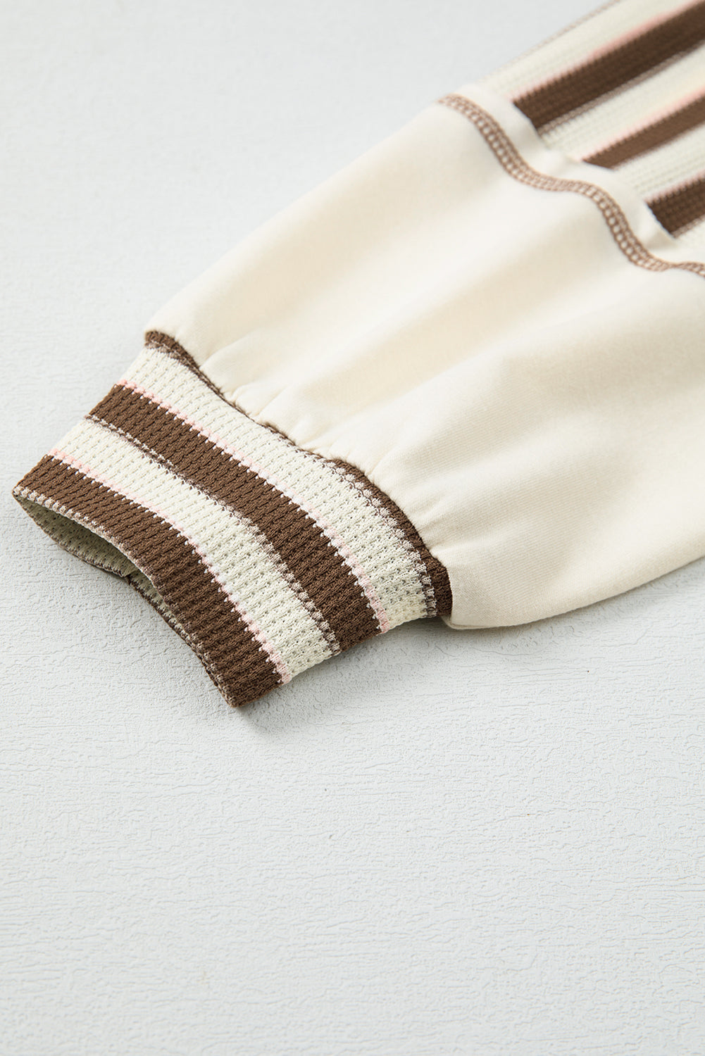 Close-up of a cream-colored glove with brown striped cuffs on a light gray background