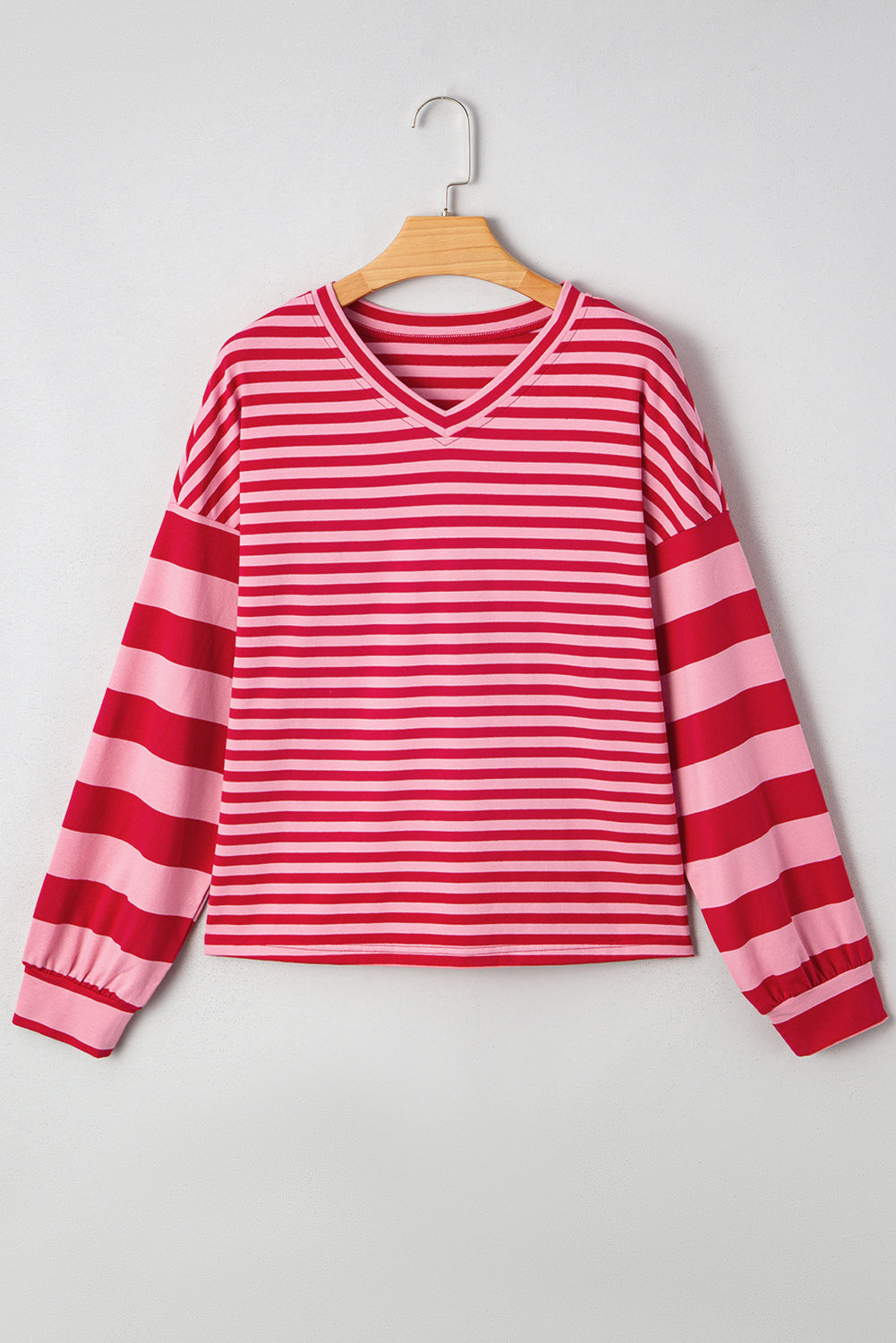 Red and pink striped long-sleeve shirt on a wooden hanger against a light gray background